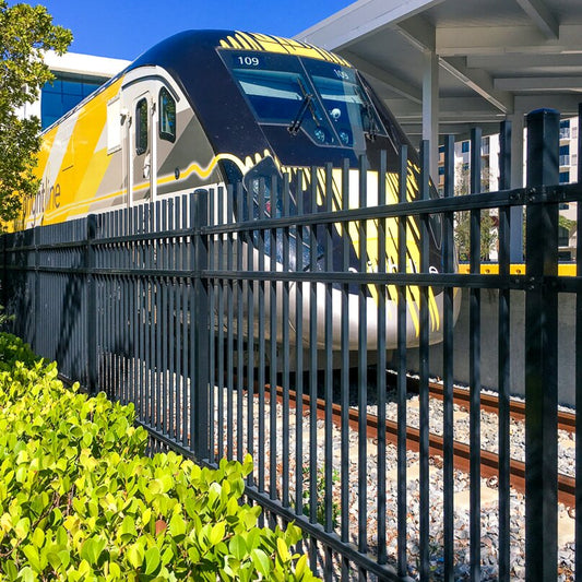 Extruded top extruded bottom commercial three rail fencing in front of the Brightline train