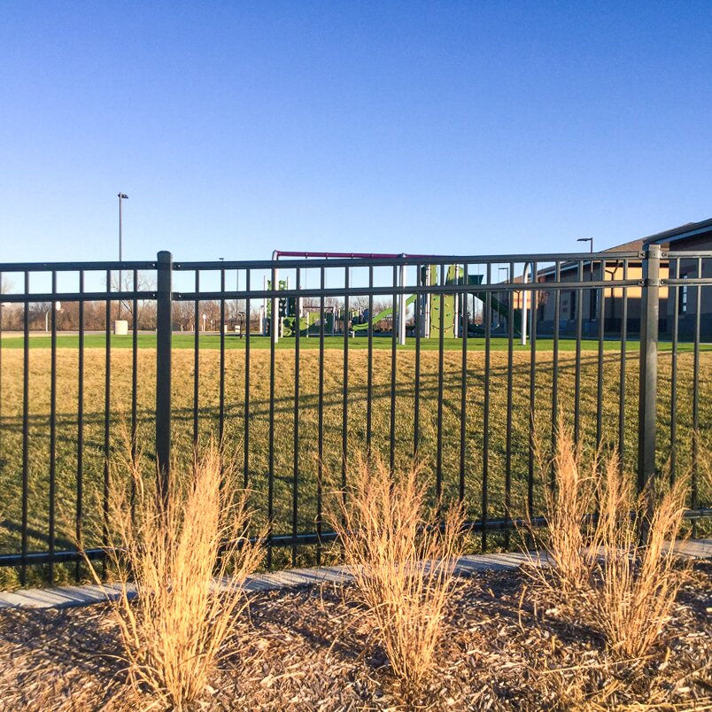 Flat top extruded bottom, three rail fencing surrounding a lawn with a playground in the distance