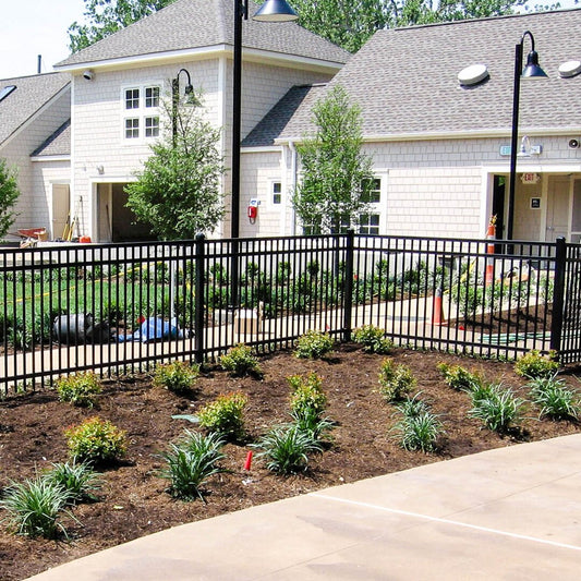 A black ornamental steel fence installed around a residential area with landscaping in front of the houses.