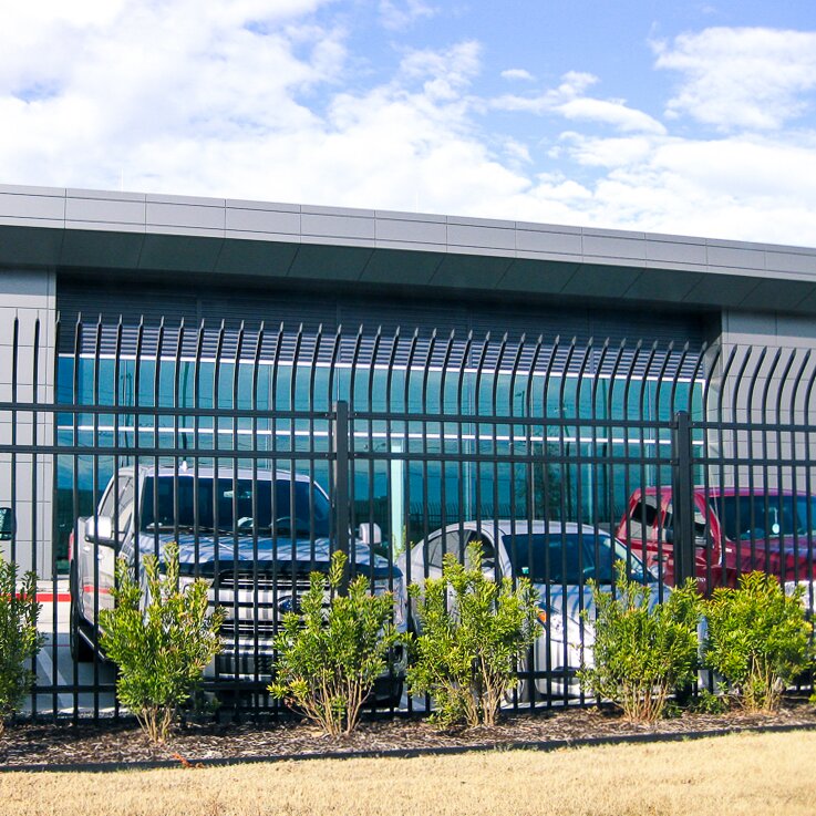 A black ornamental steel fence in front of a building with vehicles parked behind it.