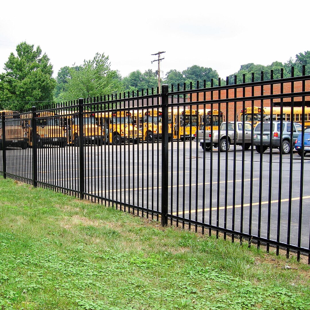 Extruded top extruded bottom, three rail, commercial fencing surrounding a public school parking lot full of buses