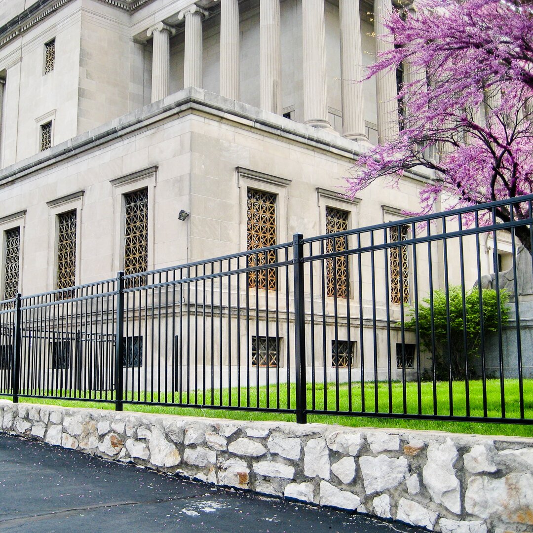 Flat top flat bottom black ornamental fencing mounted on a stone wall attached to a federal style building