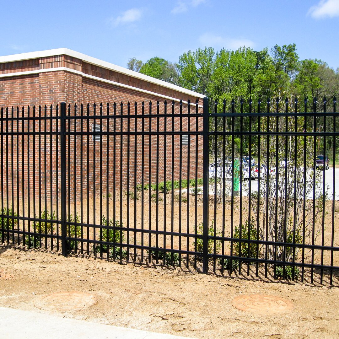 Pressed spear extruded bottom, four rail, commercial fencing surrounding a public restroom and parking lot