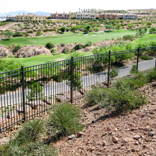 A section of Montage ornamental fence installed along a golf course, featuring black metal pickets and a green landscape in the background.