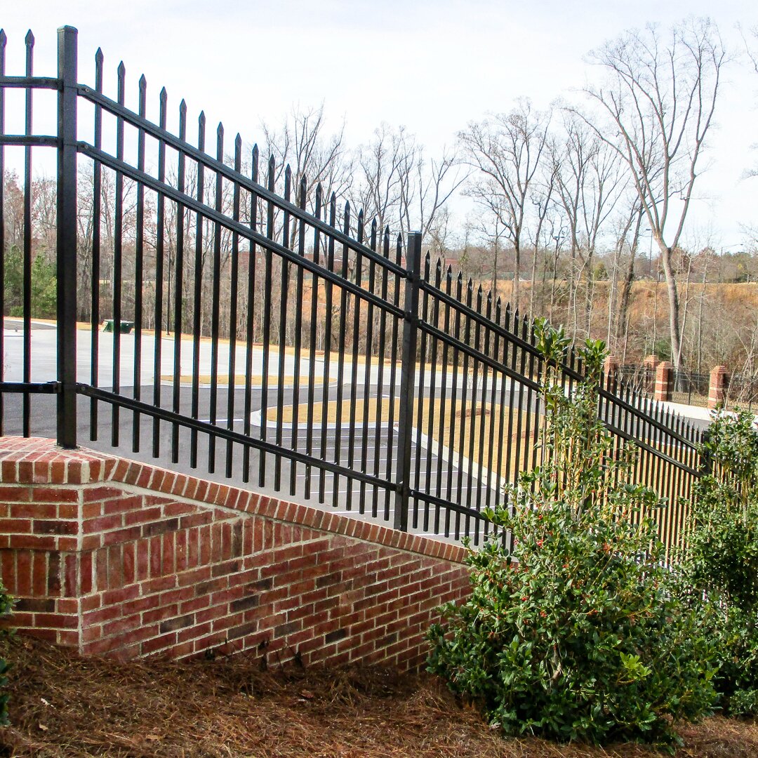 Pressed spear extruded bottom, three rail fencing, mounted on a brick wall on a slope overlooking a parking lot