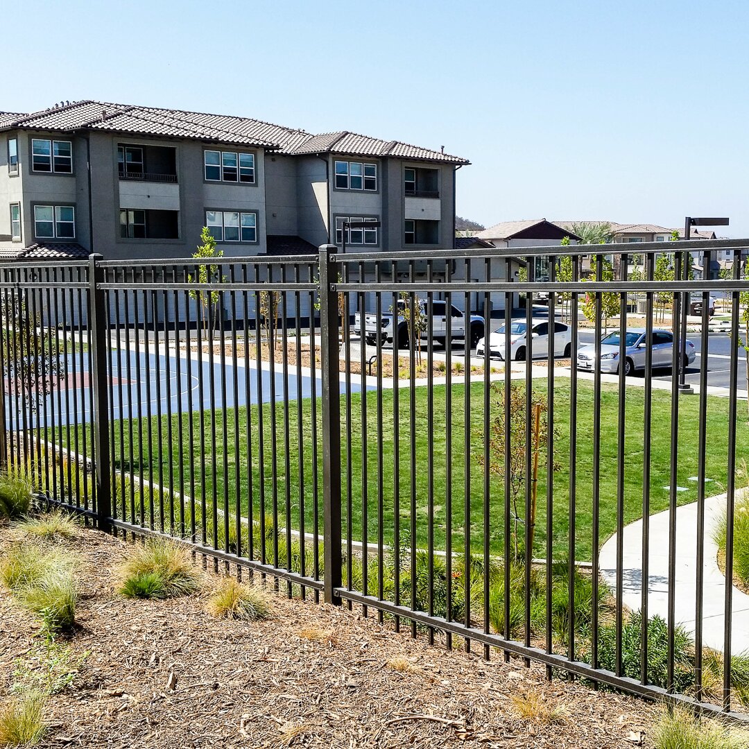 Flat top extruded bottom, three rail fencing surrounding a basketball court and parking lot at an apartment building